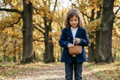 Petite fille en manteau bleu marine intemporel et jean droit dans un parc aux feuilles d'automne, illustrant les vêtements classiques pour enfants